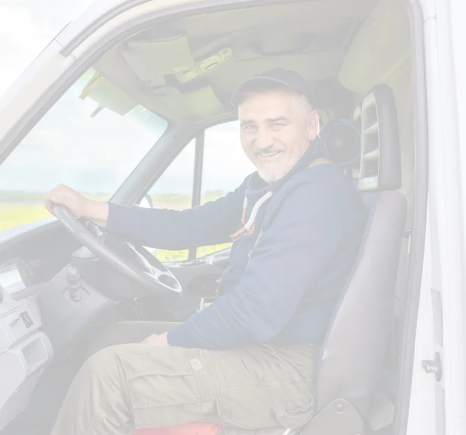 Smiling man in a cap sitting in a vehicle driver's seat, looking out the open door.