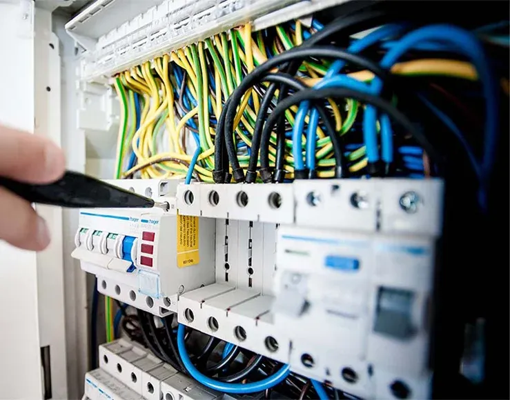 Hand using a tool to adjust wires in an electrical panel with various colored cables and circuit breakers.